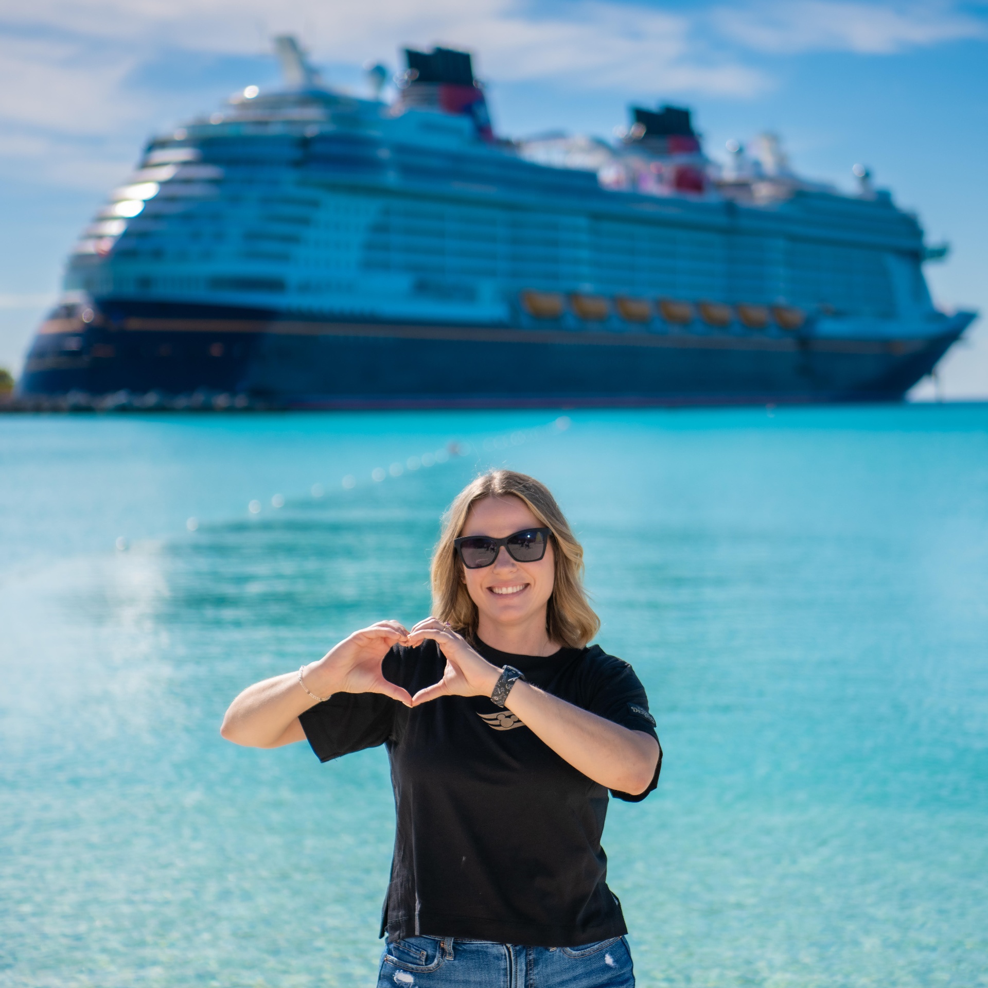 Michelle making a heart with her hands in front of a Disney cruise ship