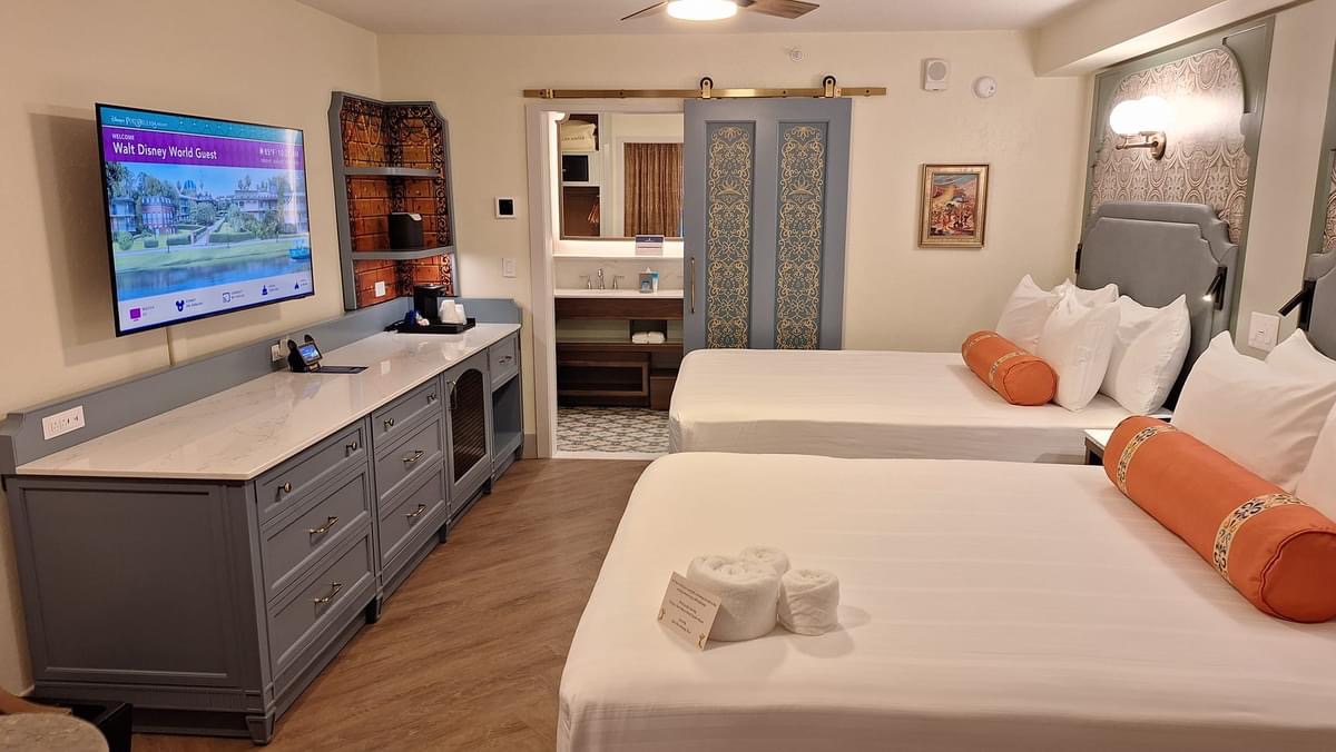 A Disney resort hotel room with two queen beds and a welcome message on the TV