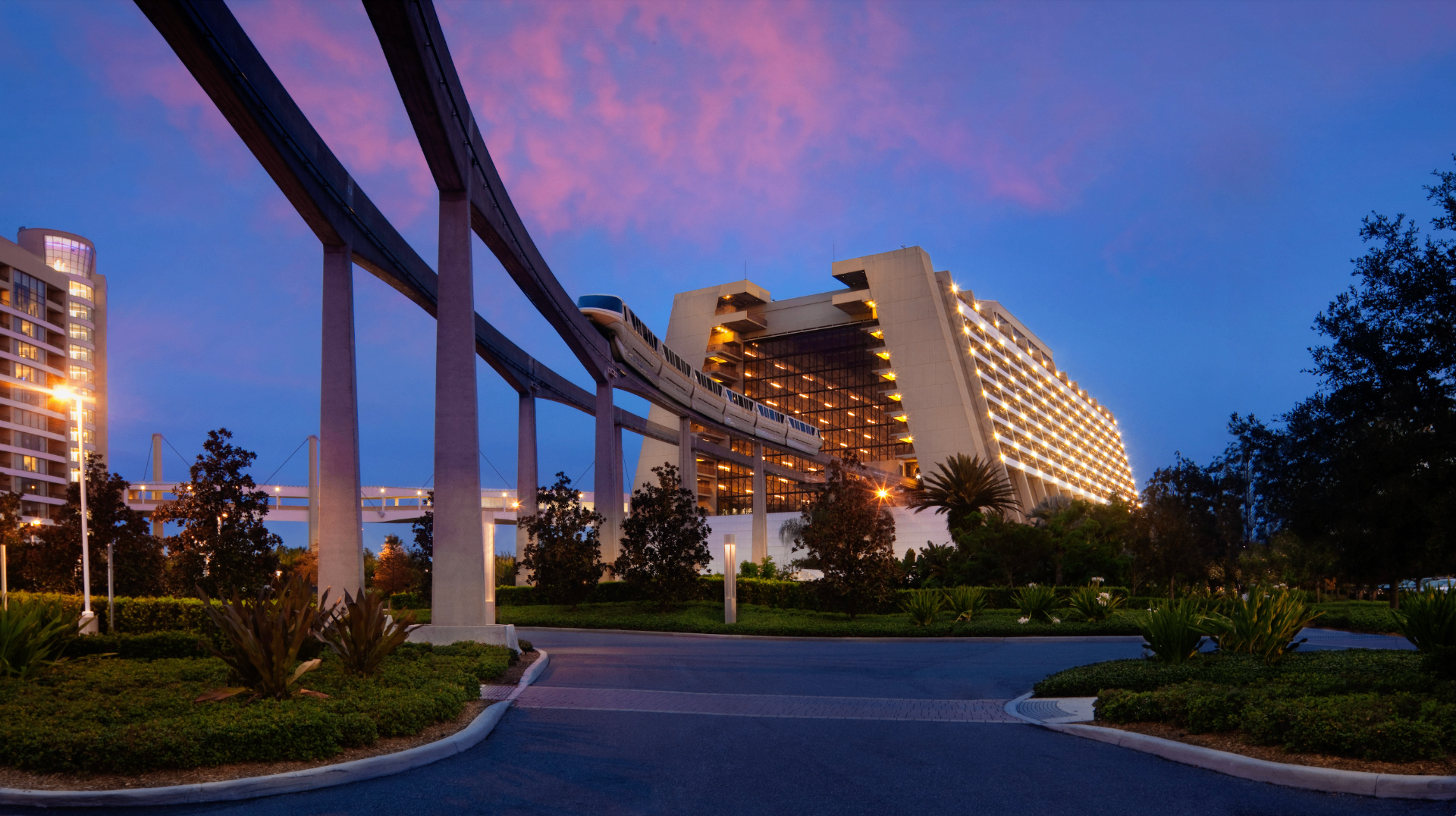 Disney's Contemporary Resort at dusk with the monorail gliding past under a pink and purple sky