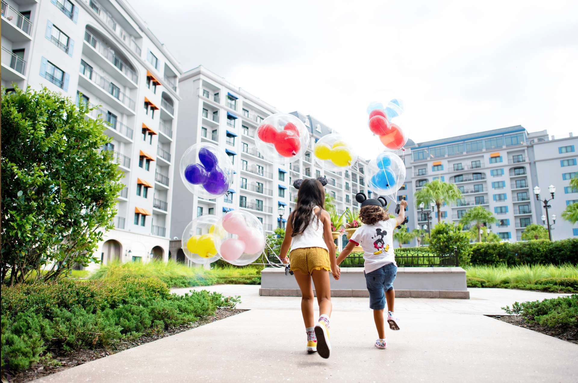 Two children with Mickey balloons running toward a Disney resort